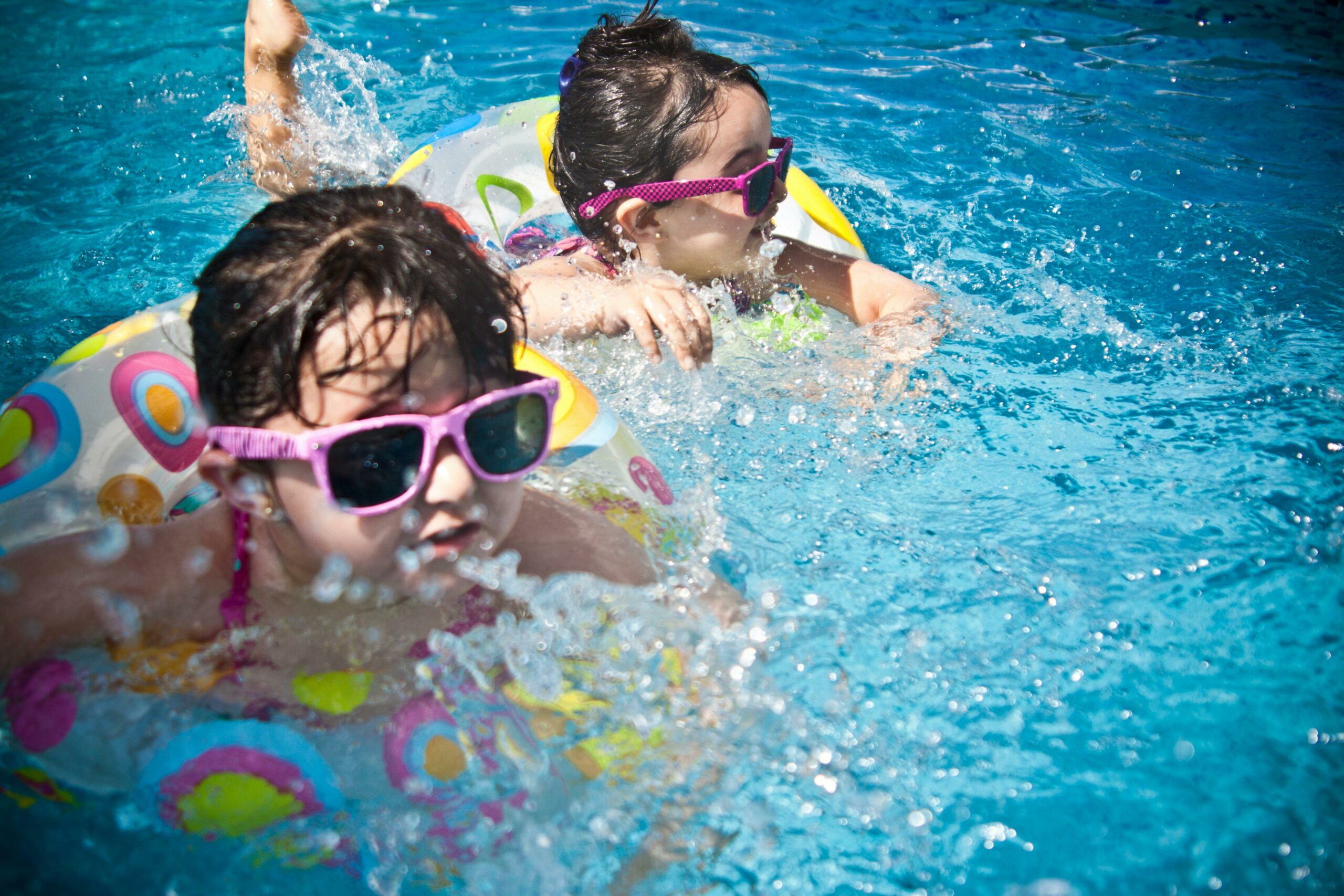 Kids wearing sunglasses, swimming in a pool with floaties